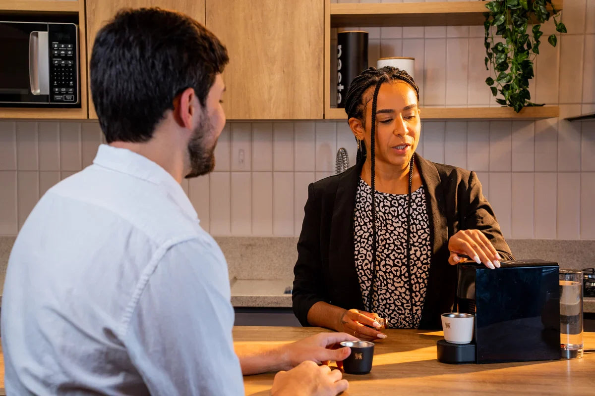 Dois amigos fazendo uma pausa para tomar café no meio do ambiente de trabalho.