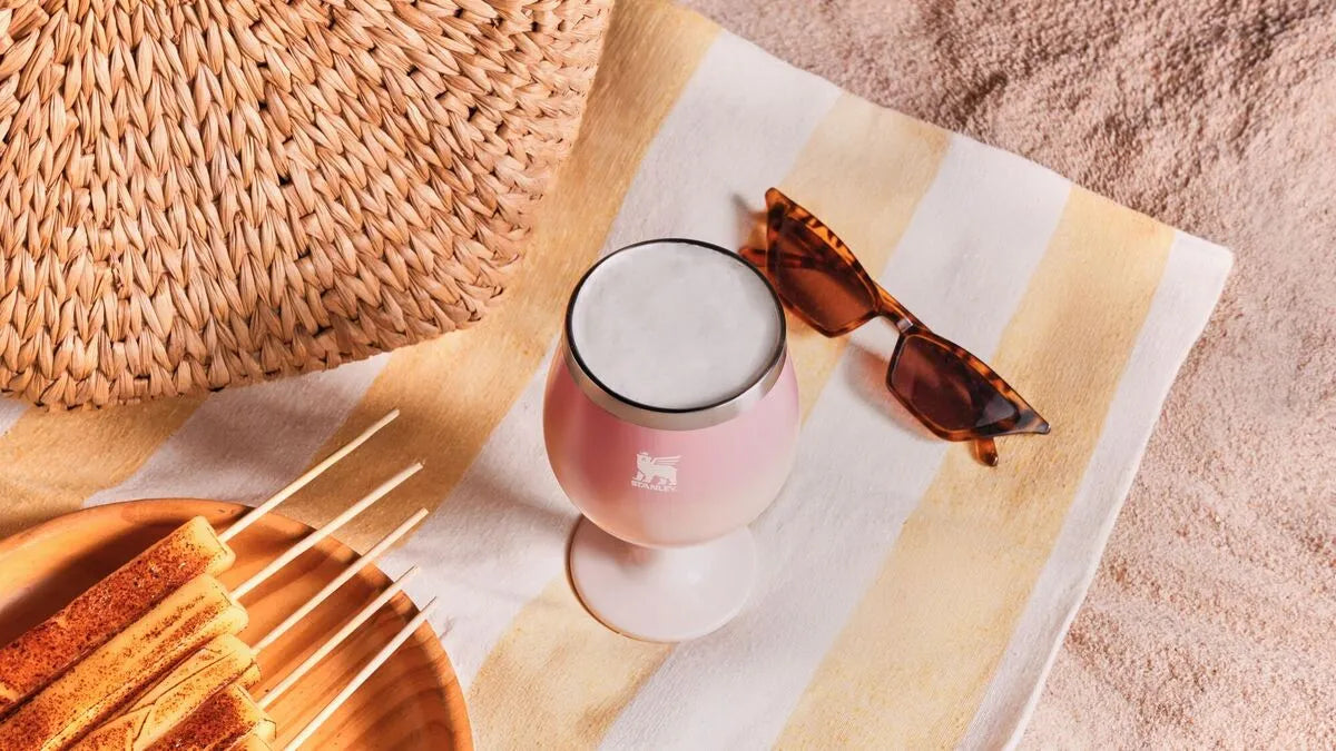 Um Cocktail Glass Stanley visto de cima perto da areia da praia representando a sobrevivência na orla com as dicas de manutenção contra salitre e areia.