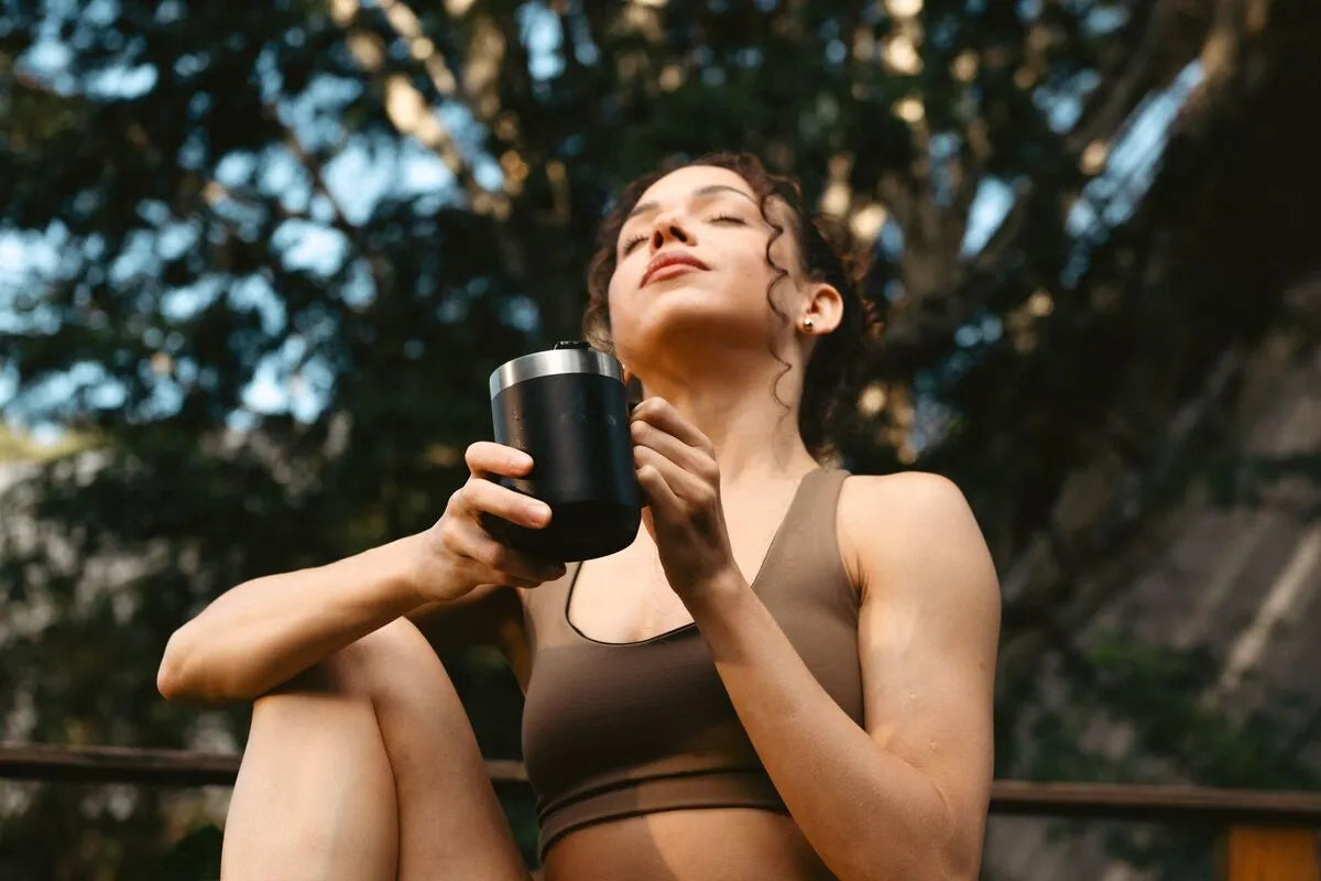 Uma mulher segurando uma caneca Stanley enquanto realiza uma viagem consciente com dicas de ecoturismo.