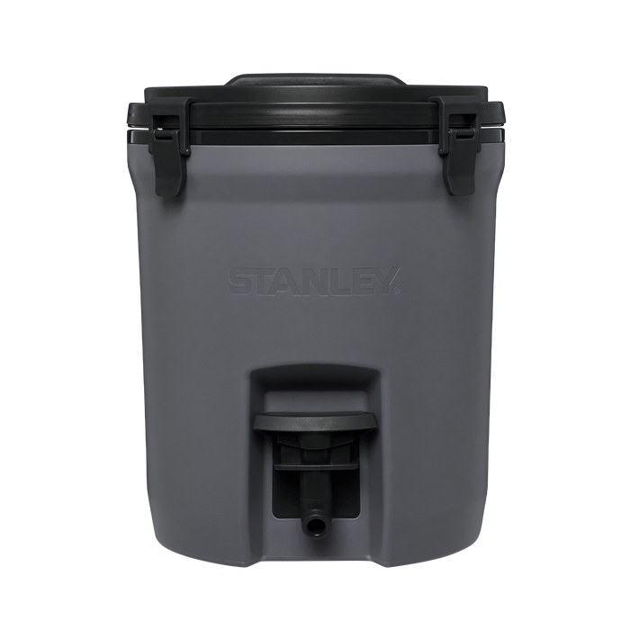 Cooler térmico cinza escuro com tampa preta e torneira inferior para dispensar líquidos. Marca "STANLEY" em relevo na frente. Design robusto e material resistente.